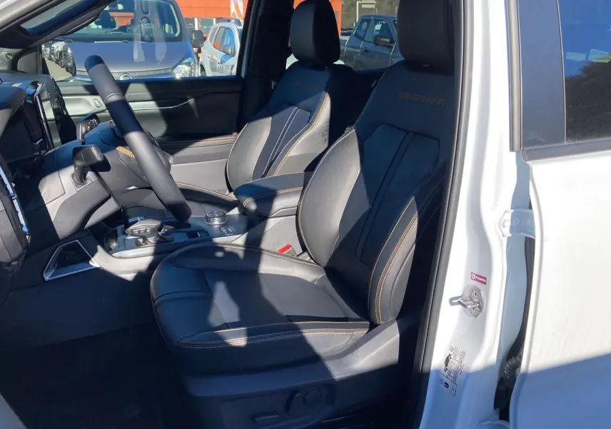 Vue intérieure côté conducteur du Ford Ranger Wildtrak blanc glacier, sièges cuir noirs avec surpiqûres orange et logo Wildtrak brodé.