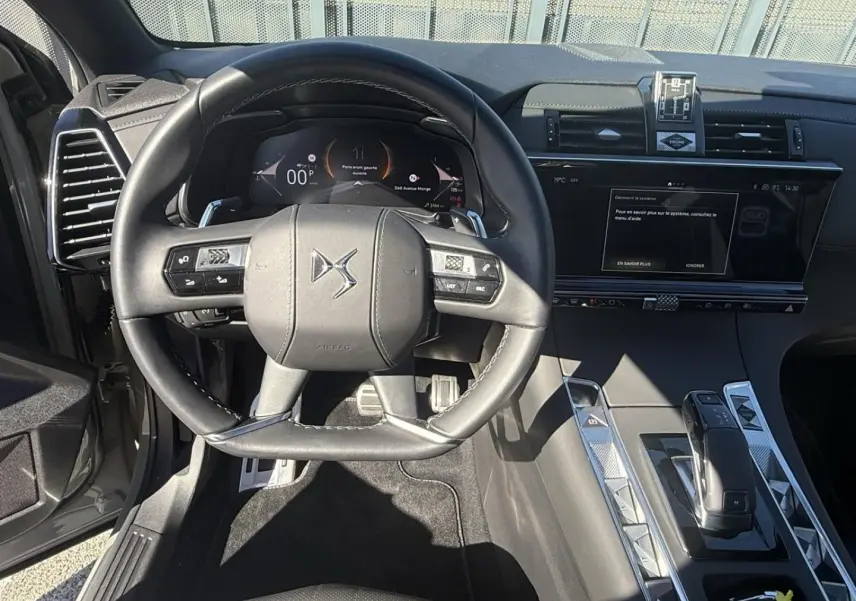 Vue intérieure centrée sur le volant et la console d'une DS7 1.5 HDI 130cv gris métal, avec tableau de bord digital et écran tactile.