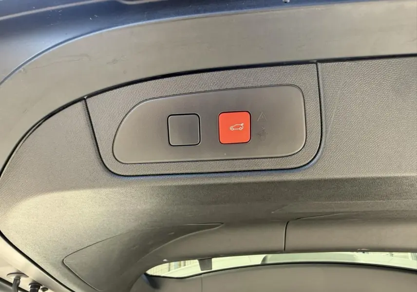Gros plan sur le bouton d'ouverture du coffre rouge à l'intérieur du hayon du DS7 gris métal 2025.
