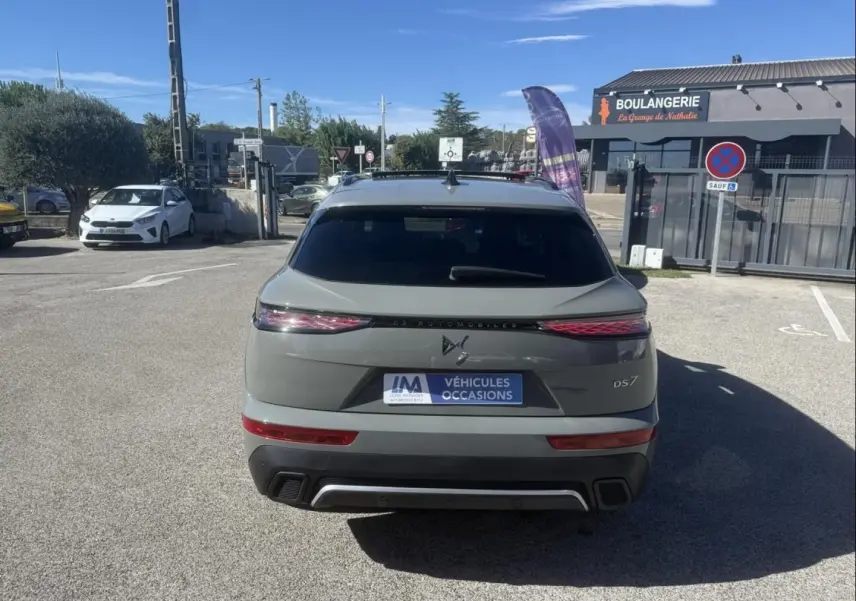 Vue arrière d’un DS7 gris métal 2025 avec feux allongés et logo DS distinctif, stationné devant une boulangerie.