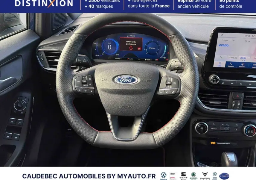 Vue intérieure centrée sur le volant perforé avec surpiqûres rouges et tableau de bord numérique du Ford Puma 2024.