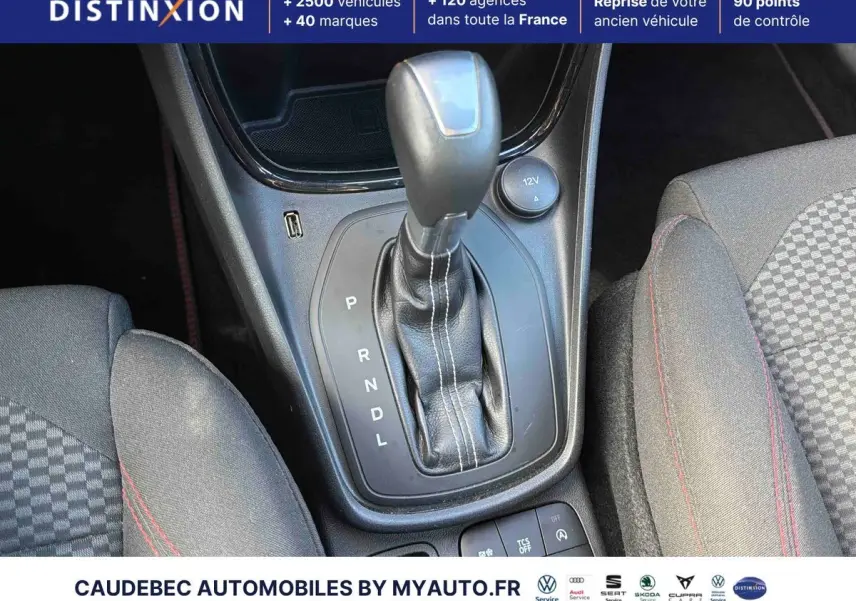 Gros plan sur le levier de vitesses automatique gainé cuir avec surpiqûres rouges, sièges sport à motifs et coutures rouges visibles.