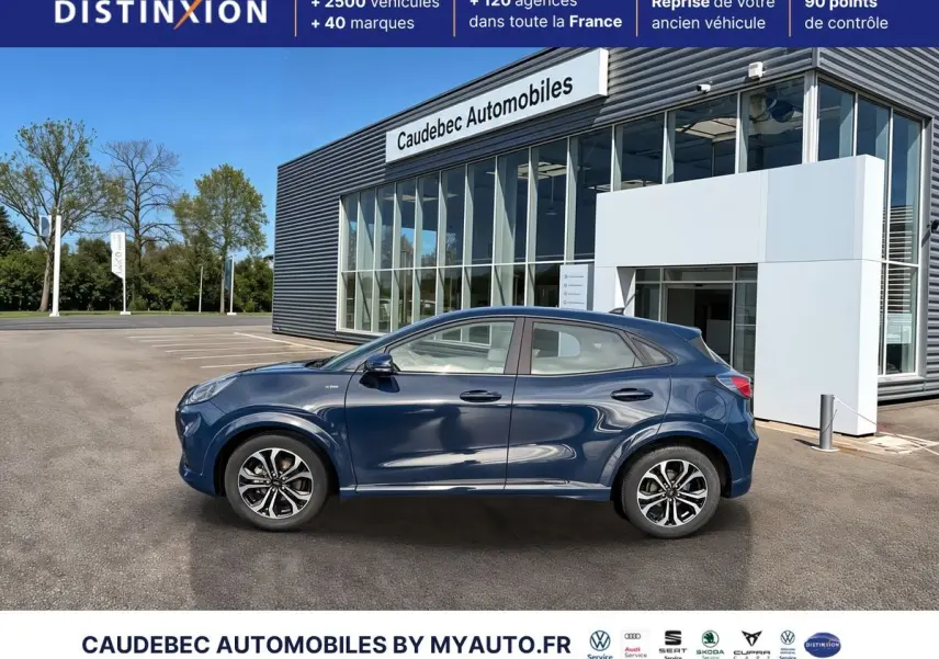 Ford Puma bleu en profil droit, avec jantes alliage 17 pouces et arches couleur carrosserie, devant un showroom.