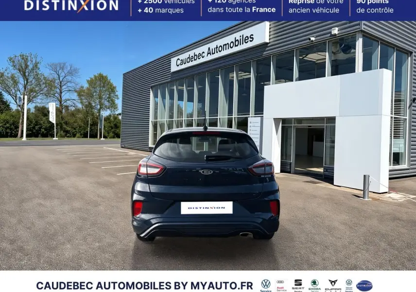 Vue arrière d'une Ford Puma 2024 bleue stationnée devant un bâtiment moderne de Caudebec Automobiles.
