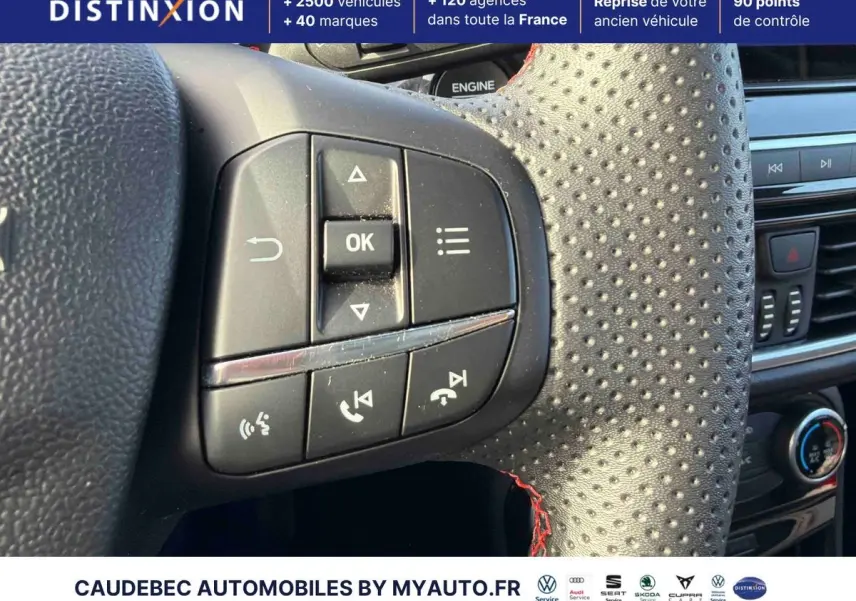 Gros plan sur les commandes multifonctions à gauche du volant perforé avec surpiqûres rouges du Ford Puma bleu.