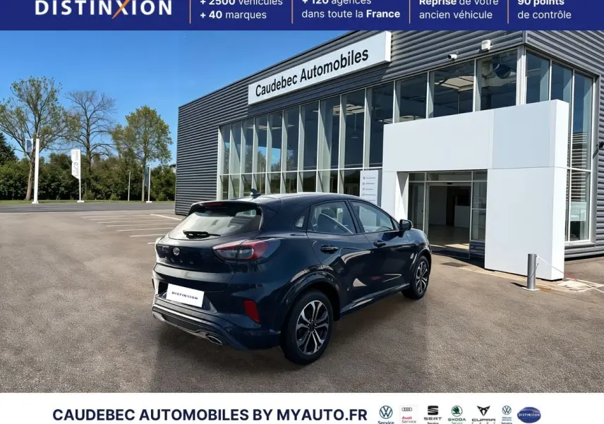 Vue 3/4 arrière droite d’un Ford Puma bleu métallisé avec jantes alliage 17 pouces devant un showroom moderne.