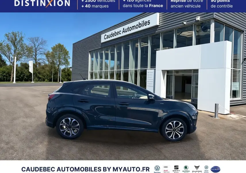 Ford Puma bleu en profil droit, avec jantes alliage 17 pouces et badges ST-Line visibles, devant un showroom.