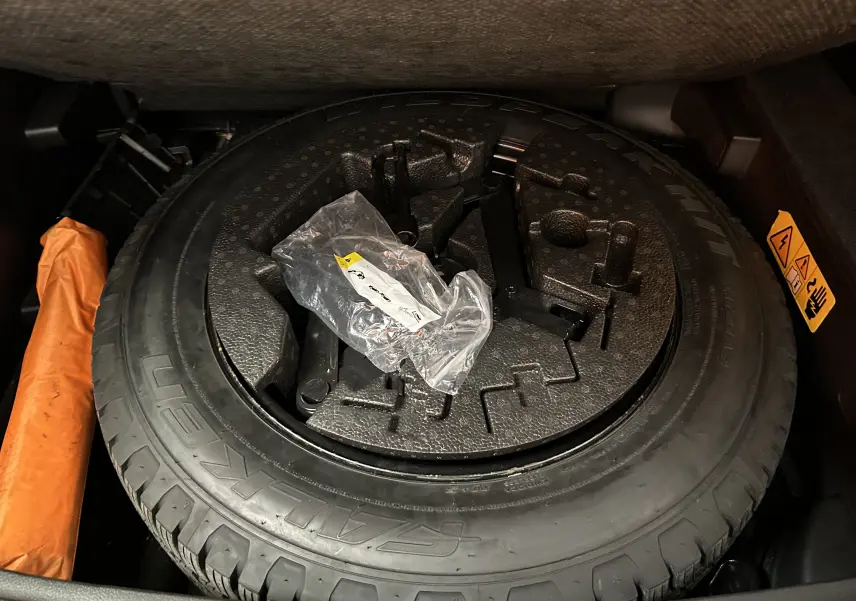 Pneu de secours et outils de bord dans le coffre du Jeep Compass gris hybride 2021, avec notice de sécurité visible.