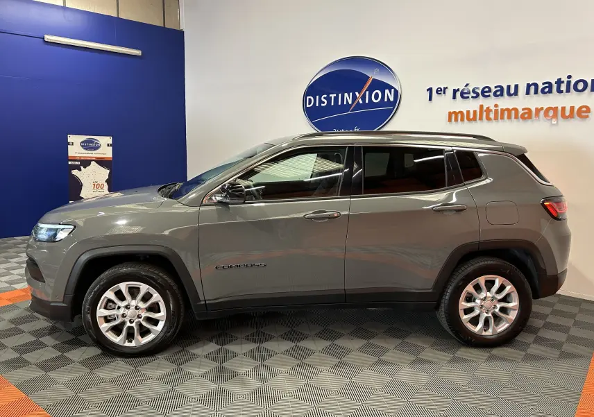 Profil côté gauche du Jeep Compass gris 2021 Limited hybride, avec jantes alliage et vitres teintées, en intérieur showroom.