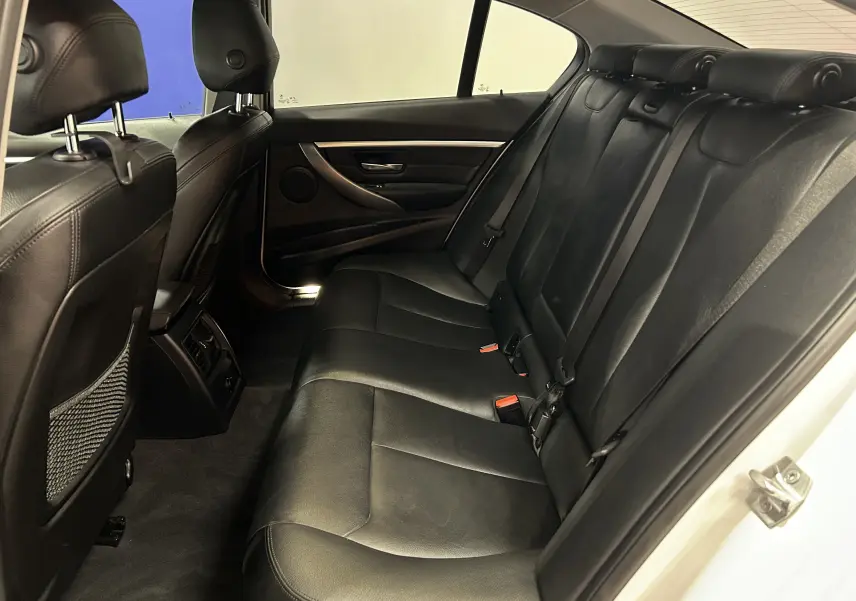 Vue intérieure arrière côté droit de la BMW Série 3 320i 2018 avec sièges en cuir noir et ceintures de sécurité visibles.
