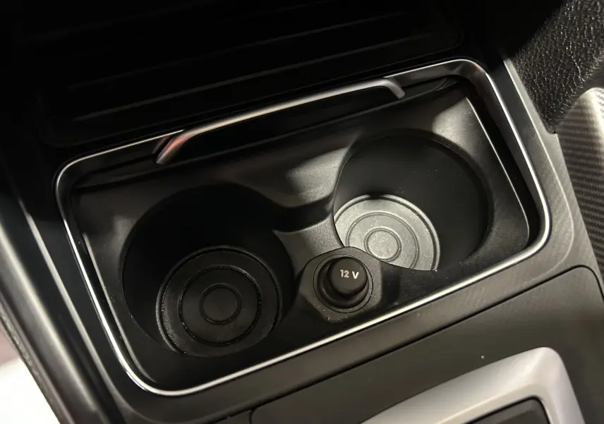 Gros plan sur les porte-gobelets noirs et prise 12V au centre de la console d'une BMW Série 3 320i blanche de 2018.