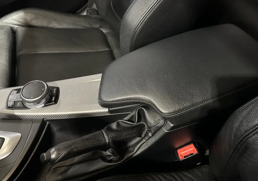 Gros plan intérieur sur la console centrale en cuir noir avec frein à main et commande iDrive d'une BMW Série 3 blanche 320i 2018.