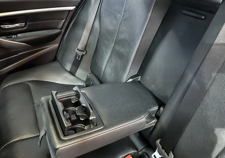 Gros plan sur la banquette arrière en cuir noir d'une BMW Série 3 320i blanche, avec accoudoir central et porte-gobelets ouverts.