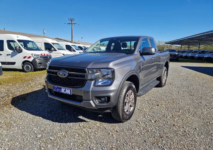 Ford Ranger Super Cabine gris carbone vu de 3/4 avant droit sur un parking en extérieur, avec calandre noire distinctive.