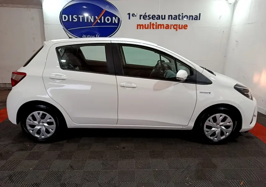 Profil côté gauche d'une Toyota Yaris blanche 2020 hybride, avec jantes argentées et badge Hybrid visible sur l'aile avant.