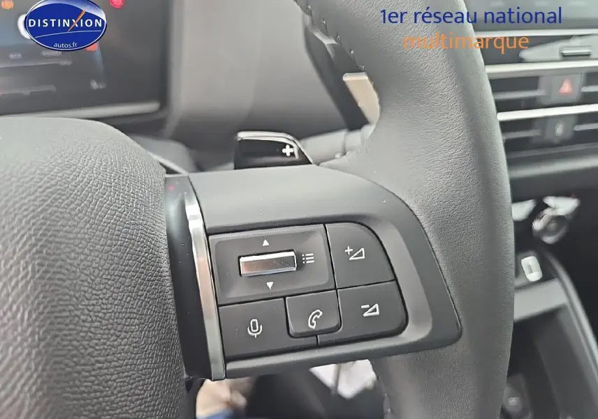 Gros plan sur les commandes au volant cuir noir de la Citroën C4 hybride 2025, avec boutons de volume et téléphone.