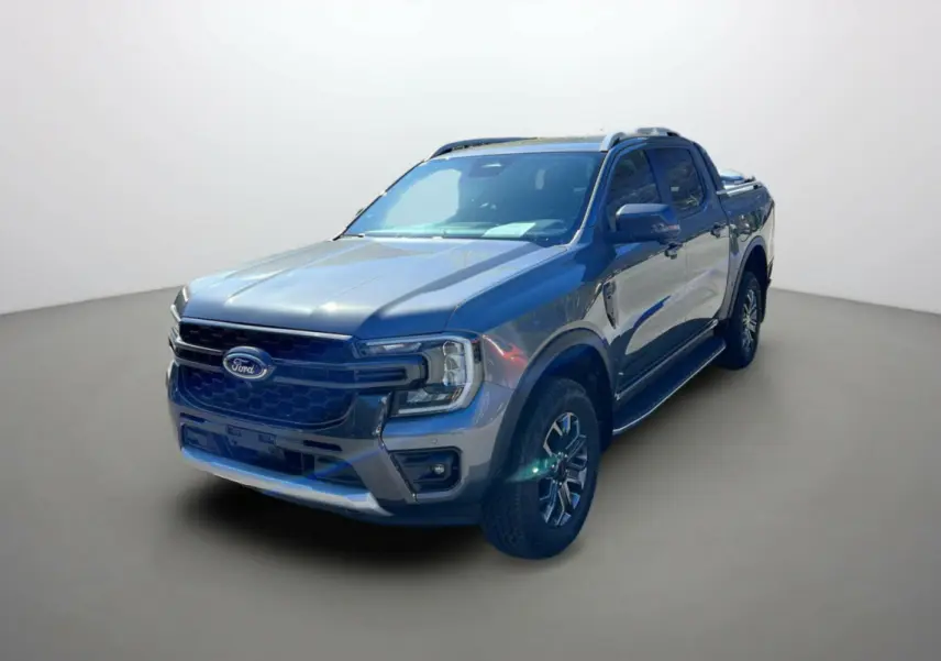 Ford Ranger Wildtrak gris carbone en 3/4 avant droit, avec barres de toit et jantes alu 18 pouces visibles.