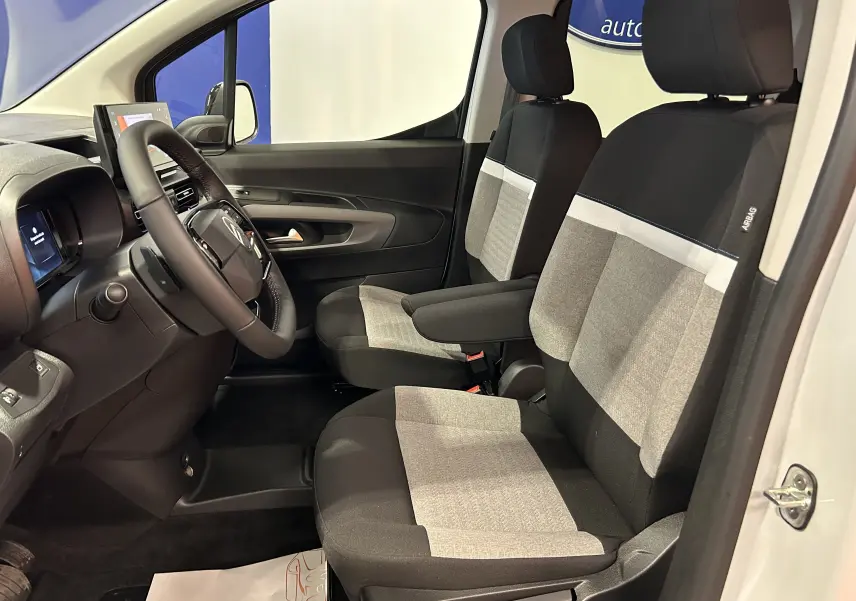 Vue intérieure côté conducteur du Citroën Berlingo Multispace 2026, sièges tissu noir et gris avec accoudoir central.