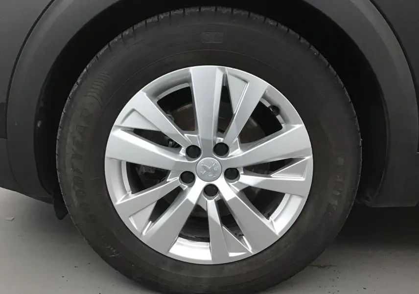Gros plan sur la jante argentée de Peugeot 5008 noire, mettant en valeur le logo lion au centre du pneu Goodyear.