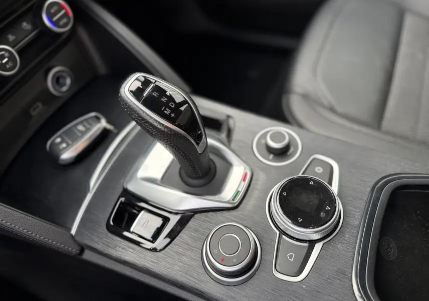 Gros plan sur la console centrale de l'Alfa Romeo Stelvio blanc, mettant en valeur le levier de vitesse automatique et les commandes circulaires.