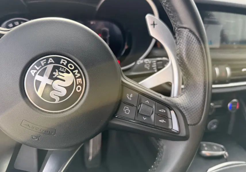 Gros plan sur le volant en cuir noir de l'Alfa Romeo Stelvio 2023, avec commandes intégrées et palettes au volant.
