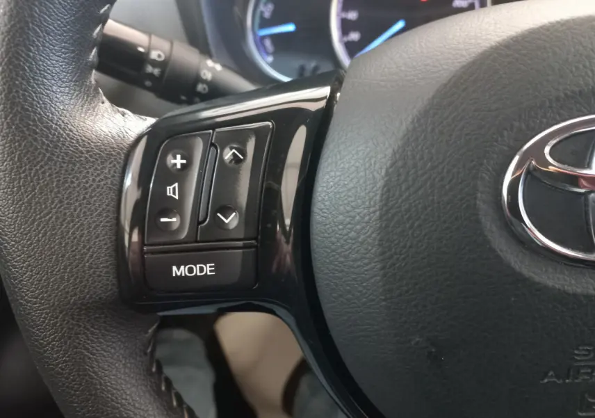 Gros plan sur les commandes gauche du volant cuir noir de la Toyota Yaris hybride 2018 avec logo Toyota visible.