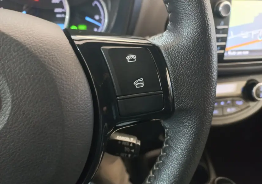 Gros plan sur les commandes téléphoniques du volant cuir noir de la Toyota Yaris hybride 2018 avec écran tactile en arrière-plan.