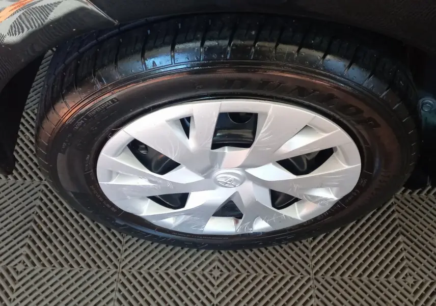 Gros plan sur la roue avant droite d'une Toyota Yaris noire, mettant en valeur la jante en plastique argenté et le pneu Dunlop.