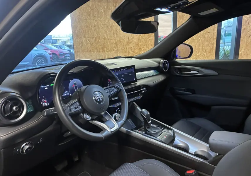 Vue intérieure côté conducteur de l'Alfa Romeo Tonale 1.3 PHEV 280 BVA TI 2023 avec tableau de bord noir et écran tactile.