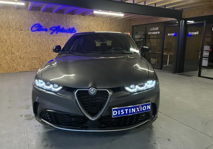 Vue frontale d'une Alfa Romeo Tonale gris foncé 2023 avec phares allumés dans un showroom moderne.