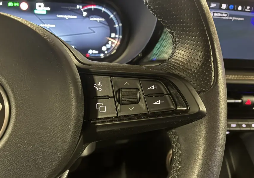 Gros plan sur les commandes du volant en cuir perforé noir de l'Alfa Romeo Tonale 1.3 PHEV 280 BVA TI gris foncé, tableau de bord numérique en arrière-plan.