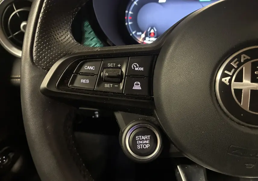 Gros plan sur le volant noir de l'Alfa Romeo Tonale 2023 avec commandes de régulateur et bouton start/stop éclairé.