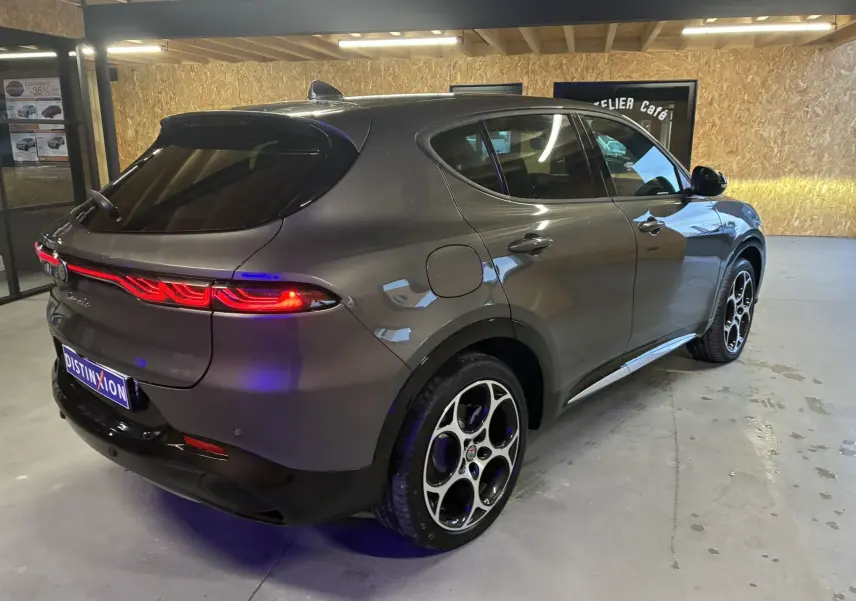 Vue 3/4 arrière droite de l'Alfa Romeo Tonale gris foncé avec feux arrière allumés et jantes distinctives en intérieur.