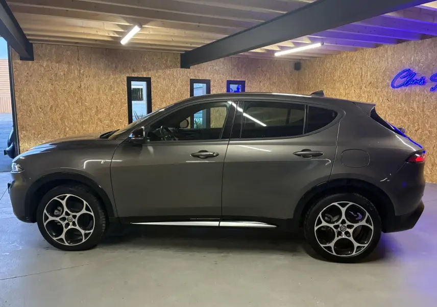 Vue de profil côté gauche d'un Alfa Romeo Tonale gris foncé hybride rechargeable, dans un garage avec mur en bois.
