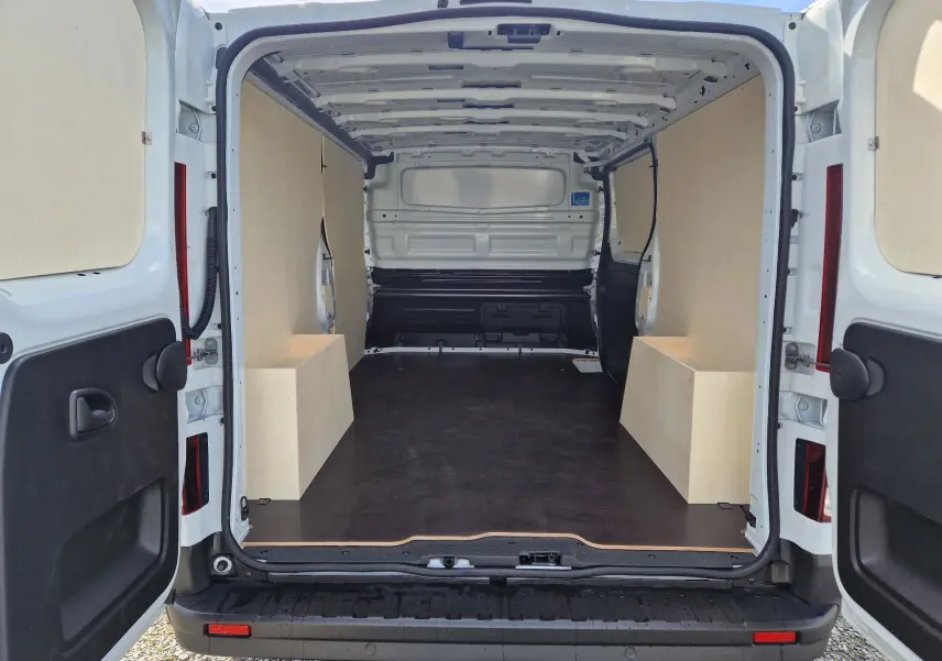 Vue arrière ouverte du Nissan Primastar blanc 2025, montrant l'intérieur cargo avec aménagements bois sur les côtés.