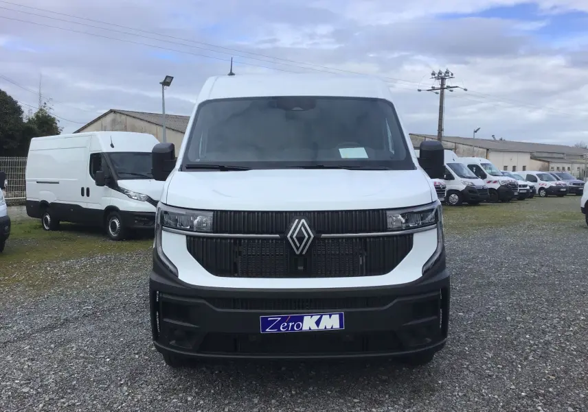 Vue avant d’un Renault Master blanc 2025 avec calandre noire et logo Renault bien visible, stationné sur un terrain gravillonné.