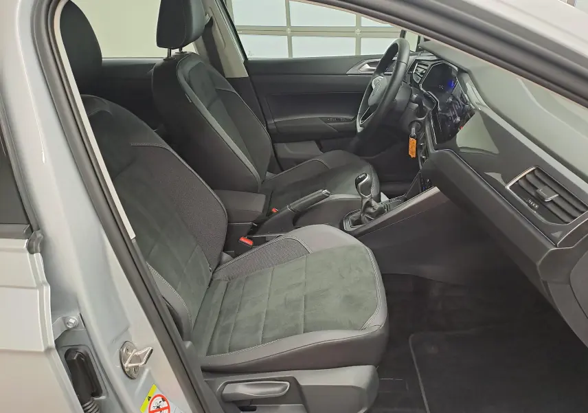 Vue intérieure côté conducteur de la Volkswagen Polo 2025 reflet d'argent, sièges noirs et levier de vitesses manuel visible.