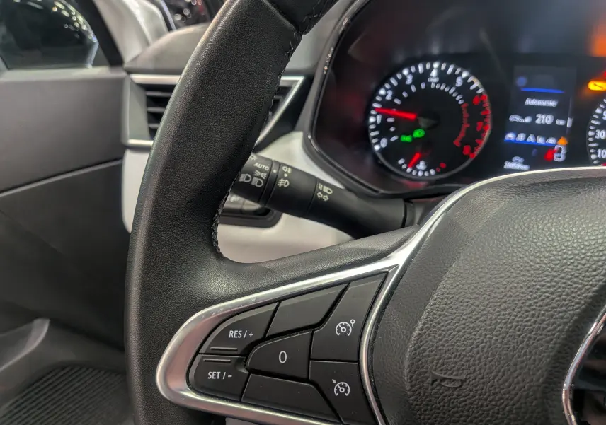 Gros plan sur le volant noir de la Renault Clio V avec commandes de régulateur de vitesse et tableau de bord lumineux.