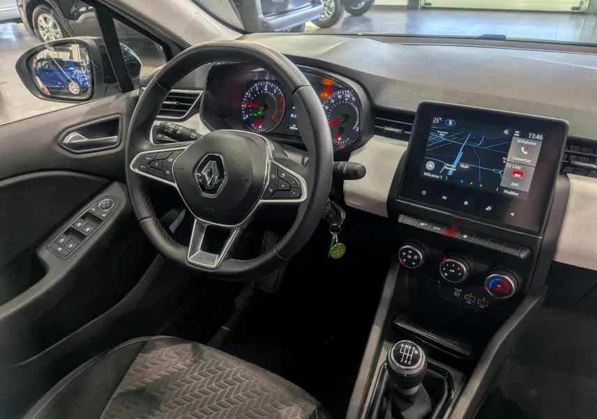 Vue intérieure côté conducteur de la Renault Clio V blanche, avec volant multifonction, tableau de bord numérique et écran tactile central.