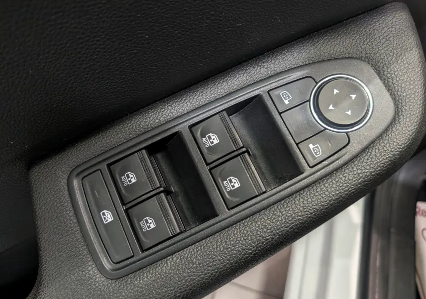 Gros plan sur les commandes de lève-vitres et réglage des rétroviseurs côté conducteur d’une Renault Clio V blanche.