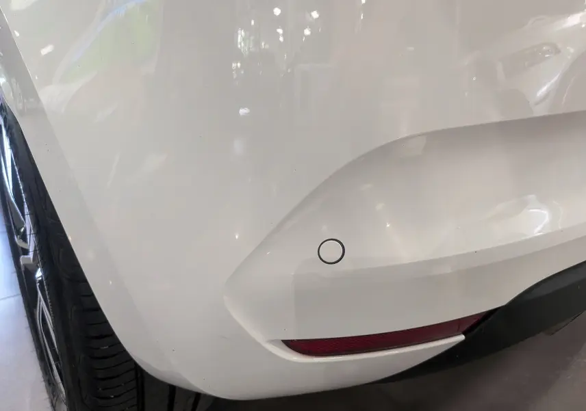 Gros plan sur le pare-chocs arrière droit blanc glacier d'une Renault Clio V TCe 100 CH GPL Evolution avec capteur de recul.