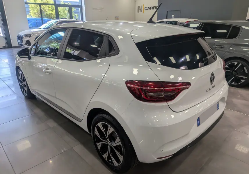 Vue 3/4 arrière droite d'une Renault Clio V blanche Glacier en showroom, avec vitres teintées et jantes alliage bicolores.