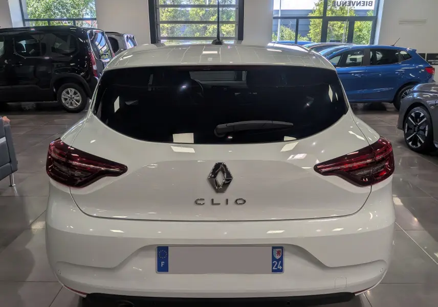 Vue arrière d'une Renault Clio V blanche Glacier, avec feux arrière LED et vitre arrière teintée, en intérieur showroom.