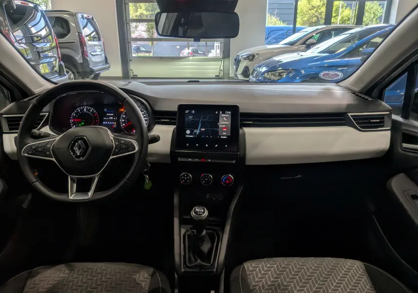 Vue intérieure avant de la Renault Clio V blanche, tableau de bord avec écran tactile et volant multifonction.