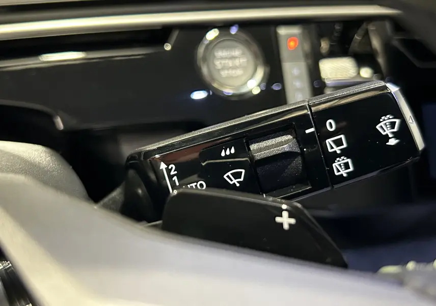Gros plan sur la commande des essuie-glaces dans l’habitacle du Peugeot 5008 Hybrid gris titane, avec bouton start visible en arrière-plan.