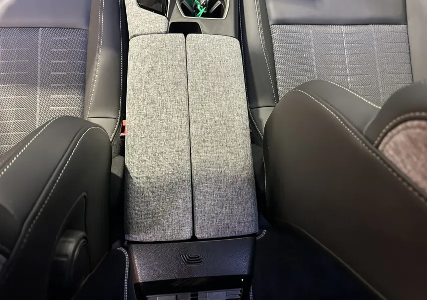 Vue intérieure centrée sur l'accoudoir central gris clair entre les sièges tissu et cuir du Peugeot 5008 Hybrid 2025.