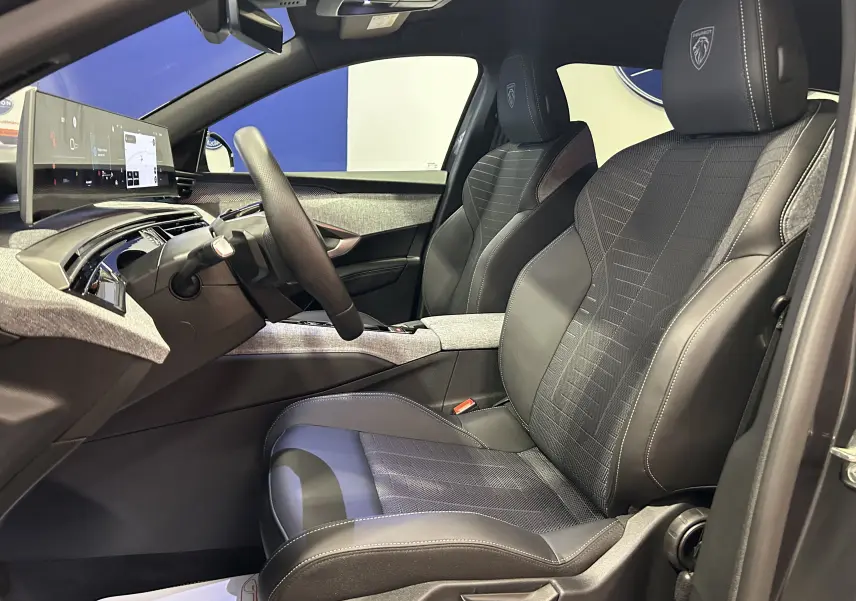 Vue intérieure côté conducteur du Peugeot 5008 Hybrid gris titane, sièges en cuir avec logo Peugeot brodé sur les appuie-têtes.