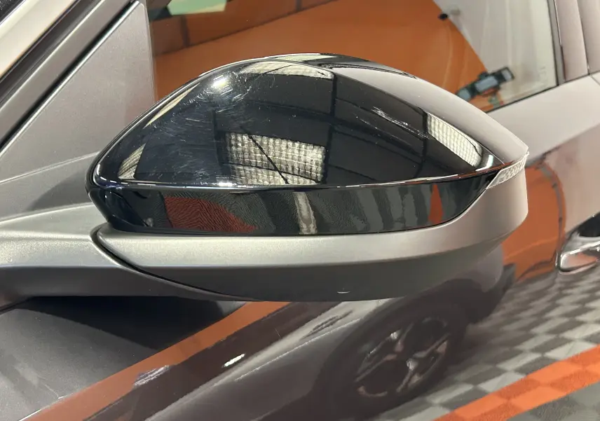 Gros plan sur le rétroviseur noir brillant côté gauche du Peugeot 5008 gris titane, avec reflet de l’environnement intérieur.