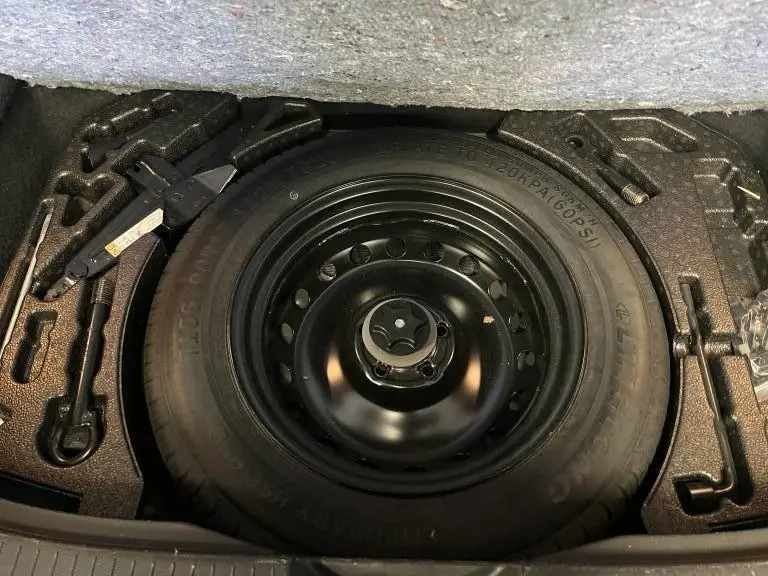 Roue de secours temporaire noire dans le coffre du Nissan Qashqai 2023 avec outils de changement intégrés.