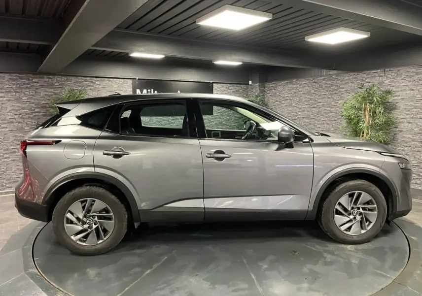 Profil côté gauche du Nissan Qashqai gris 2023 avec toit noir et jantes alliage 17 pouces en intérieur showroom.